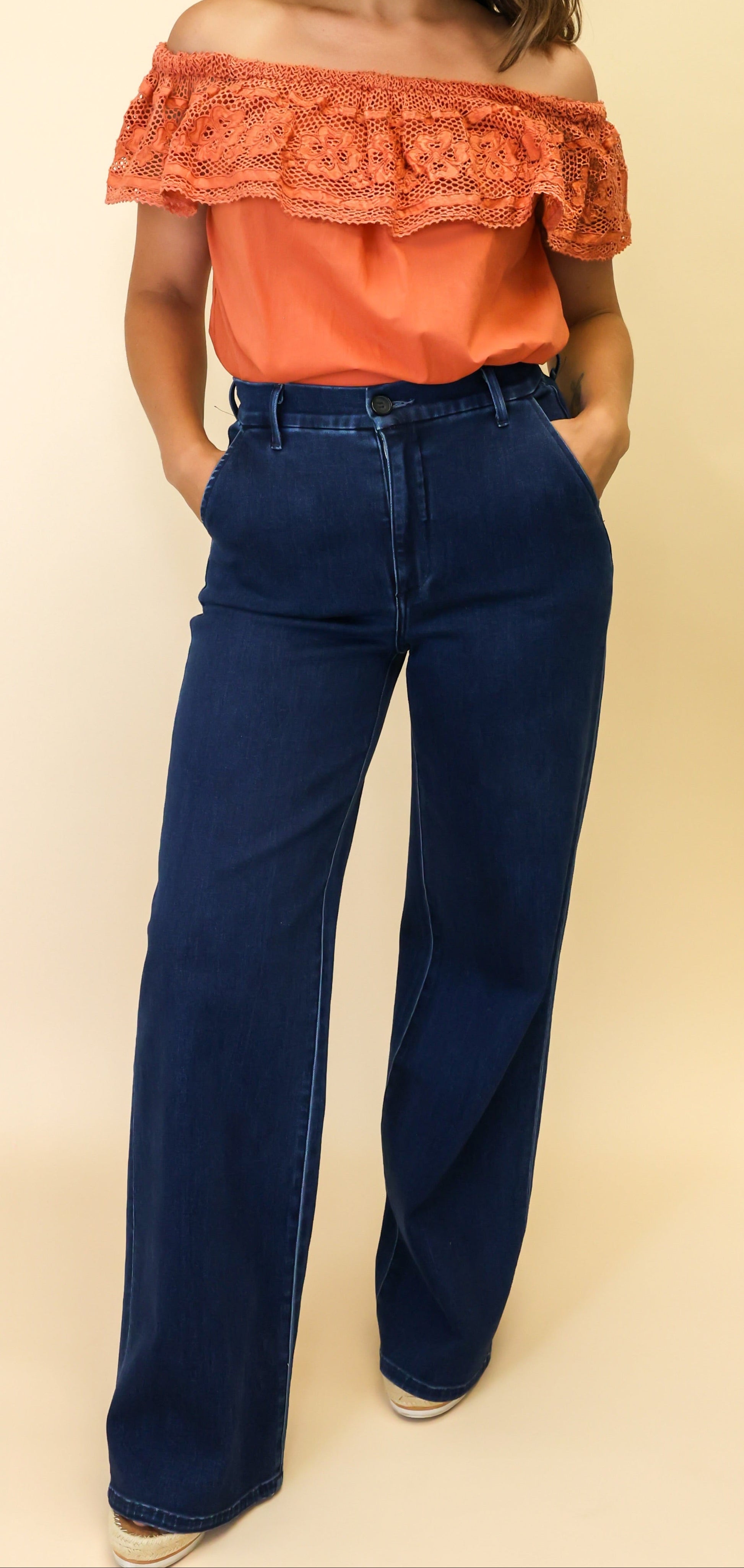 Woman wearing an orange off-shoulder top and blue jeans on a beige background