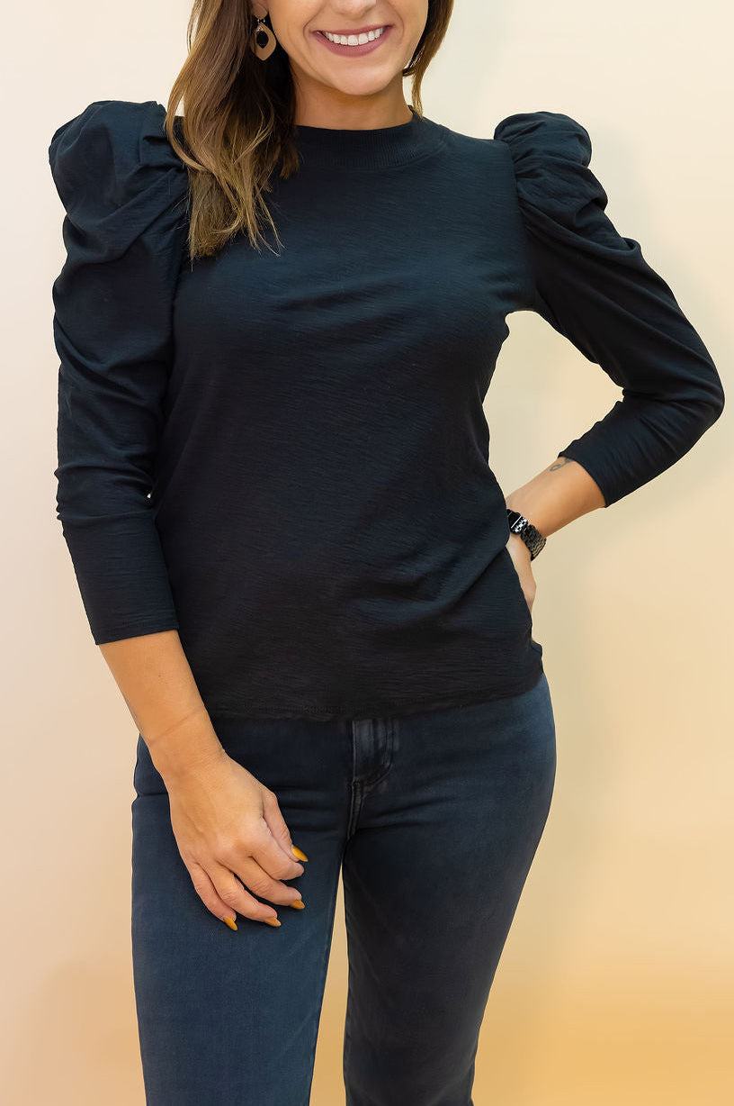 Woman wearing a black top with ruffled sleeves against a beige background