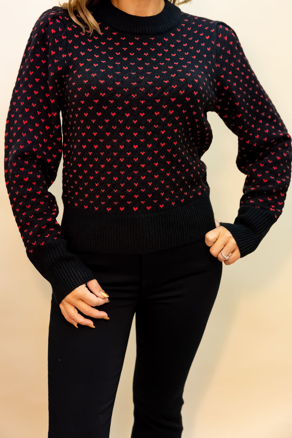 Black sweater with red pattern worn by a person on a beige background
