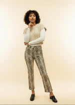Woman wearing a cream sweater and snake print pants against a beige background