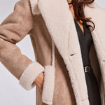 Close-up of a person wearing a beige coat with white fur lining on a plain background