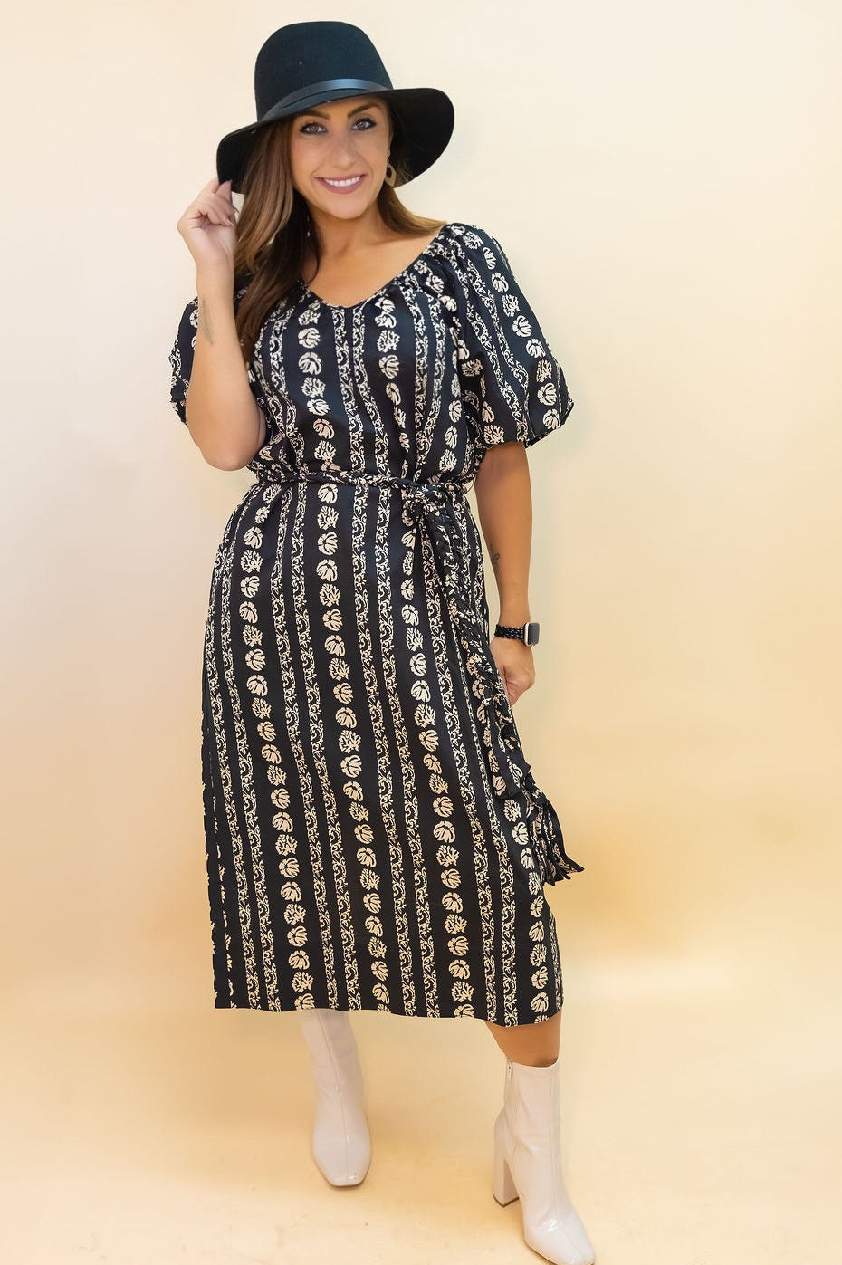 Woman wearing a black and white patterned dress with a black hat on a beige background