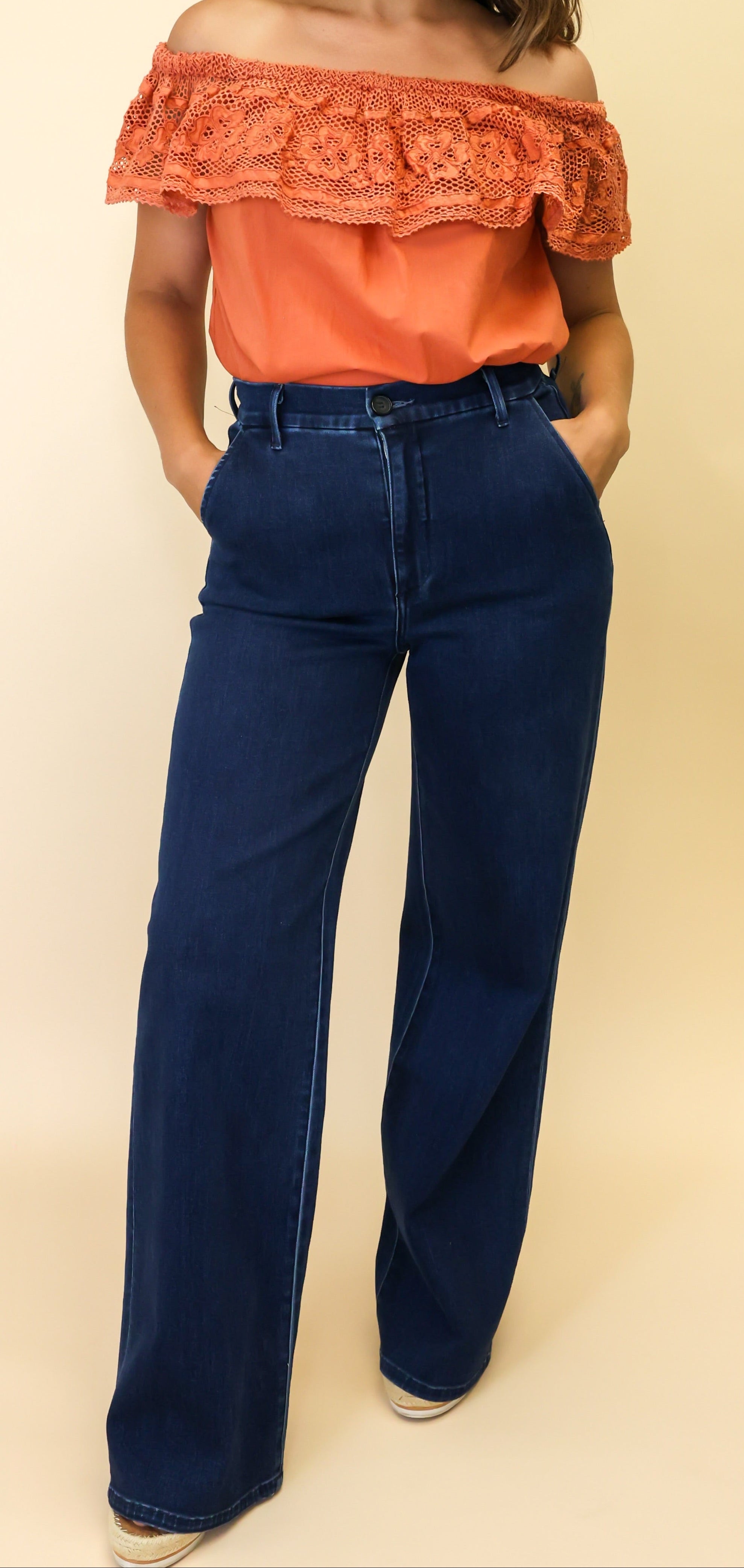 Woman wearing an orange off-shoulder top and blue jeans on a beige background