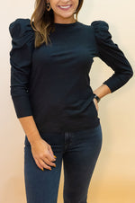 Woman wearing a black top with ruffled sleeves against a beige background