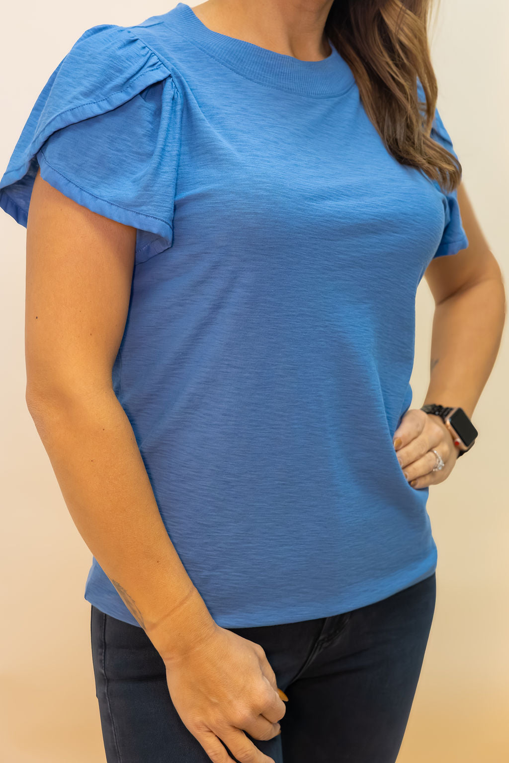 Person wearing a blue top with ruffled sleeves on a beige background
