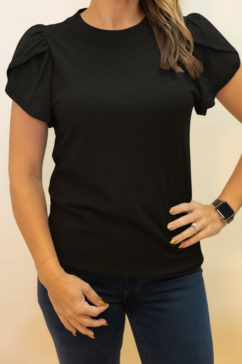 Person wearing a black
 top with ruffled sleeves against a beige background