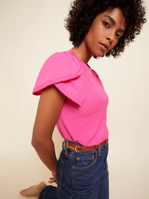 Woman wearing a bright pink top and blue jeans against a beige background