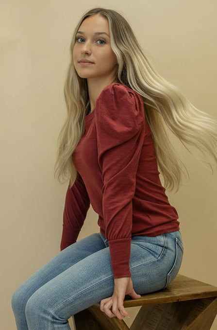 Woman sitting on a wooden bench against a beige background