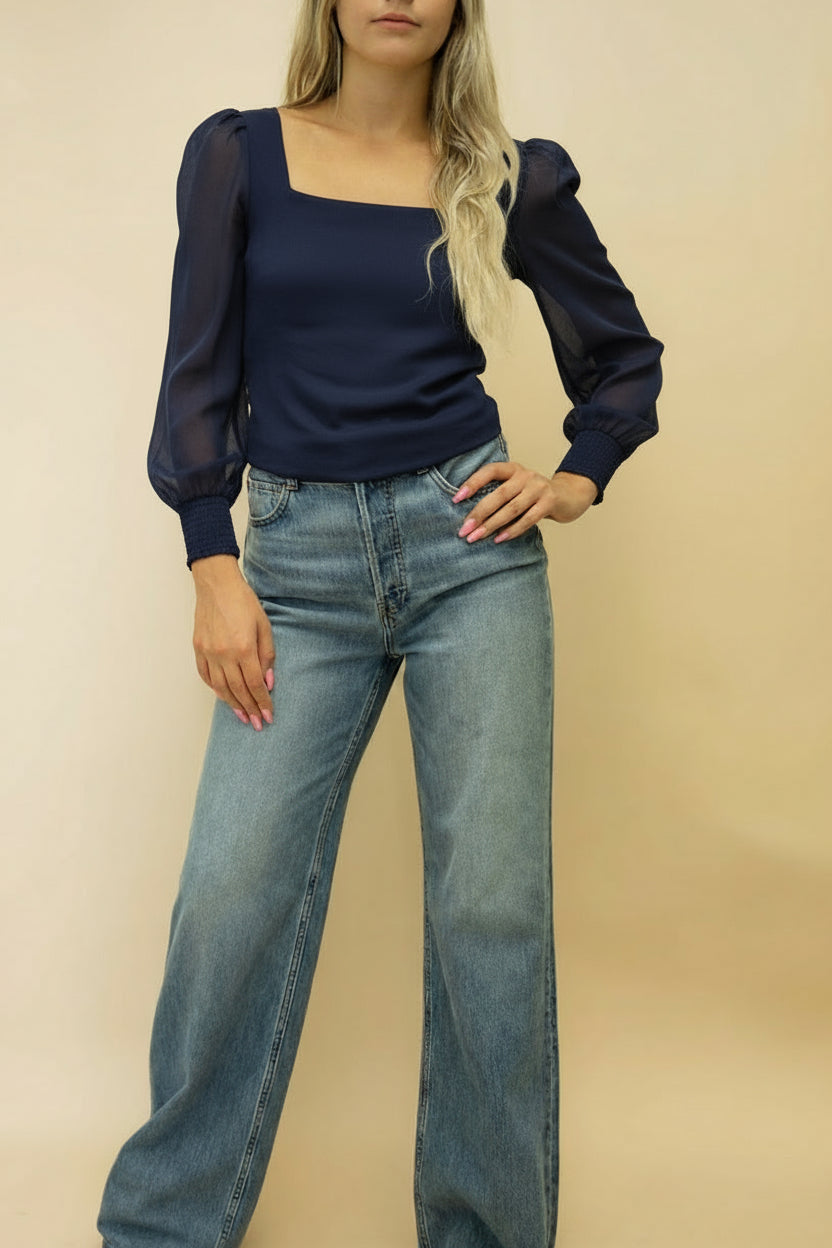 Woman wearing a white blouse and blue jeans against a beige background