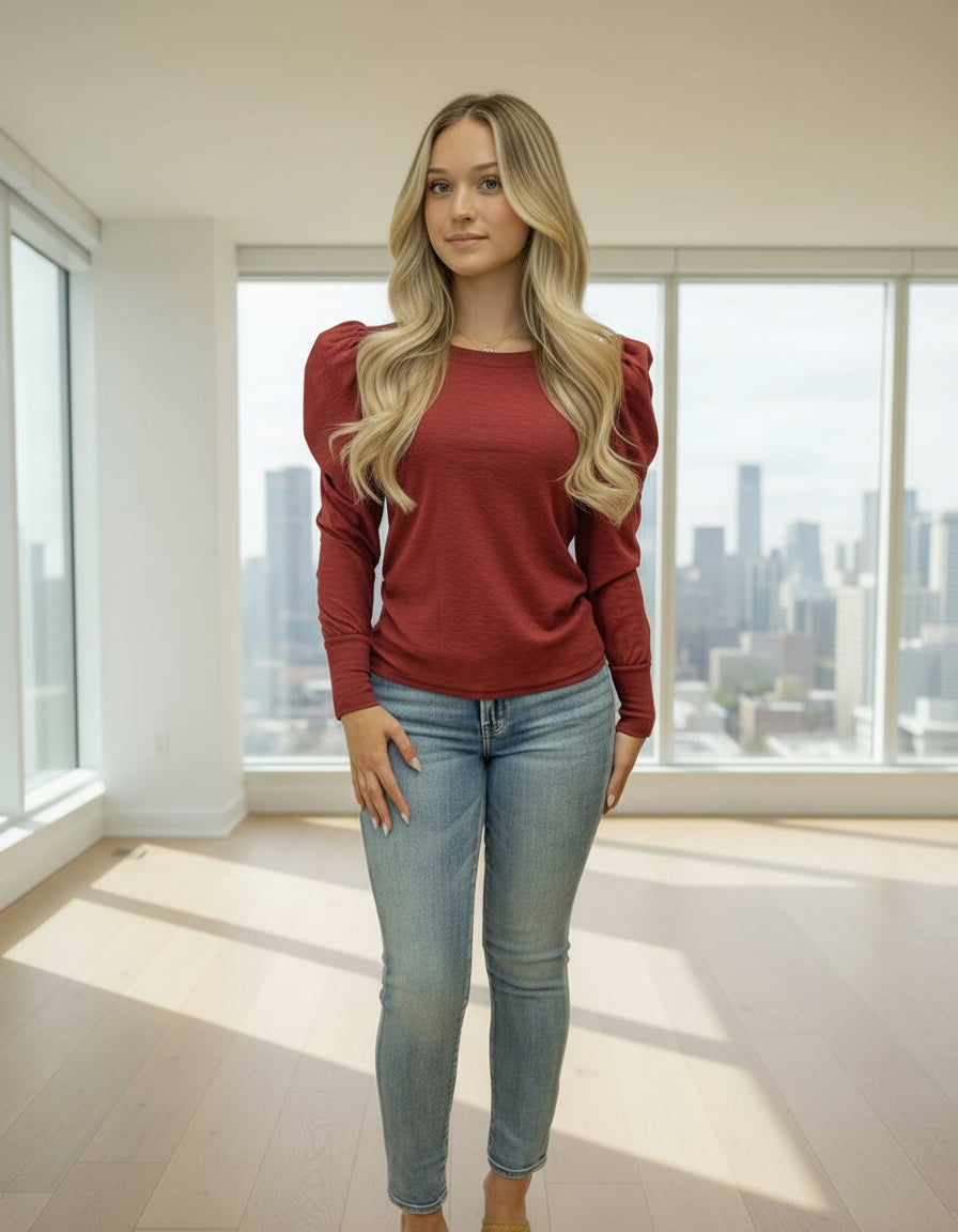 Woman wearing a red blouse with puff sleeves and blue jeans on a beige background