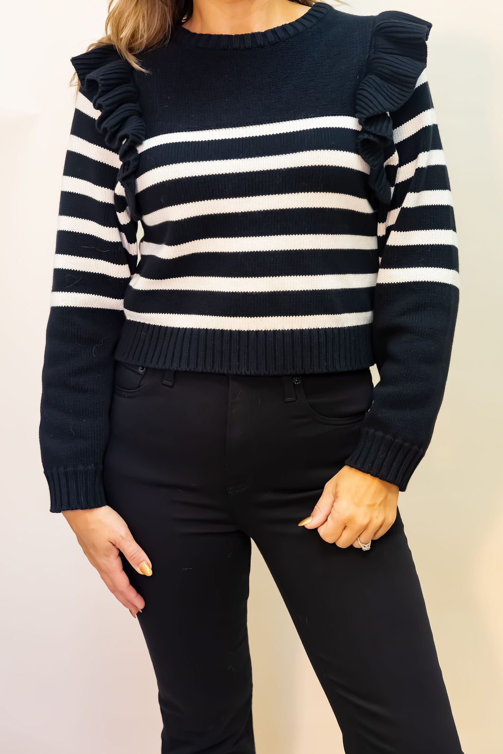 Black and white striped sweater with ruffled shoulders worn by a person against a plain background