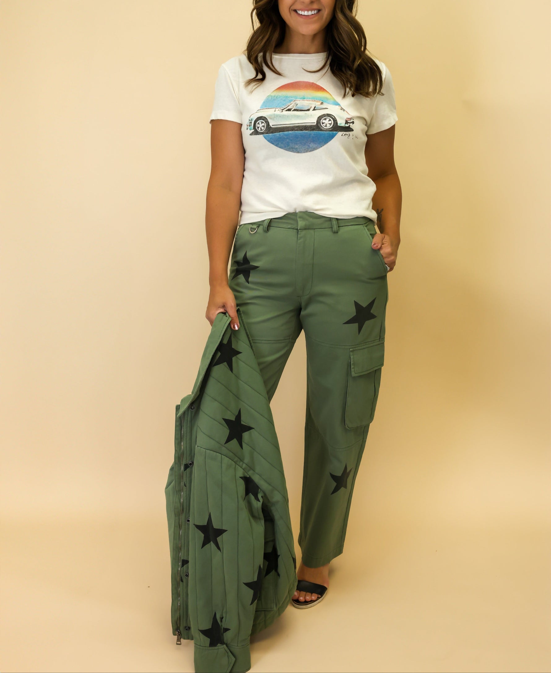 Woman wearing a white t-shirt with a graphic design and green pants with star patterns on a beige background