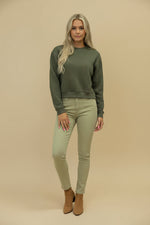 Woman wearing a green sweater and light green pants against a beige background