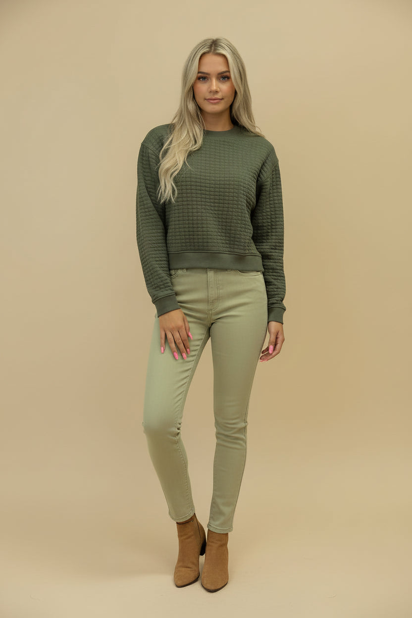 Woman wearing a green sweater and light green pants against a beige background