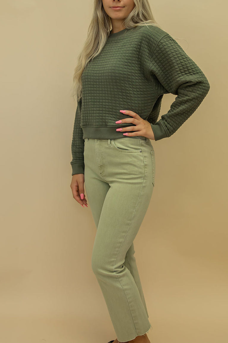 Woman wearing a green sweater and light green pants against a beige background