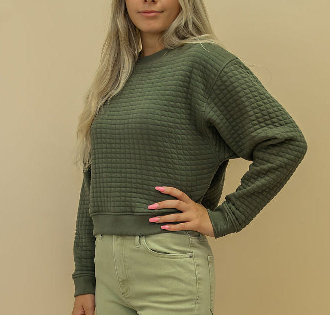 Woman wearing a green sweater and light green pants against a beige background