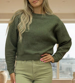Woman wearing a green sweater and light green pants against a beige background