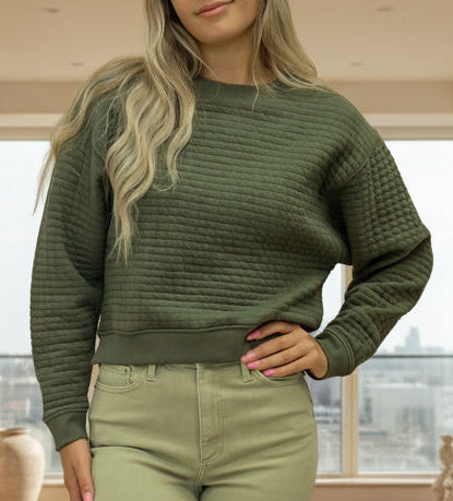 Woman wearing a green sweater and light green pants against a beige background