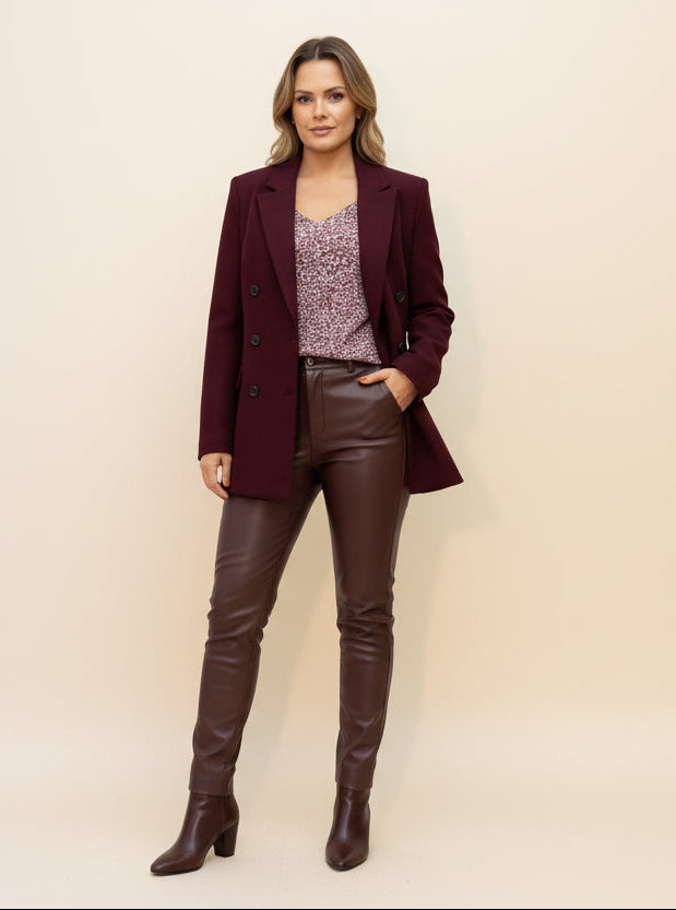 Person wearing a burgundy blazer over a patterned top and brown pants on a plain background