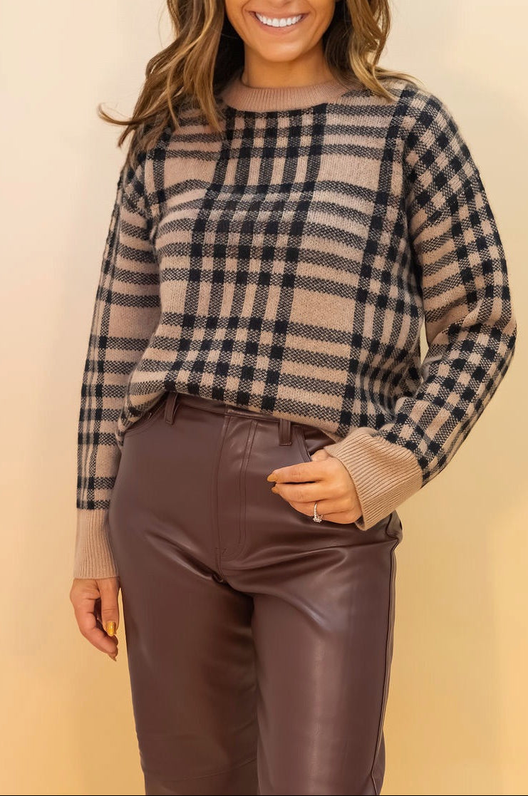 Woman wearing a plaid sweater and brown pants against a beige background