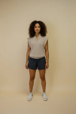 Woman wearing a beige sleeveless top and dark shorts against a beige background