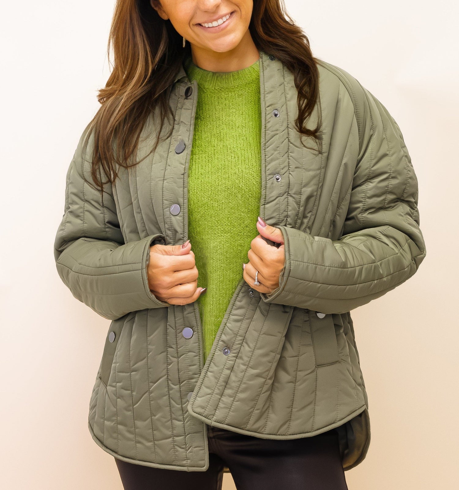 Woman wearing a green quilted jacket over a green shirt against a beige background