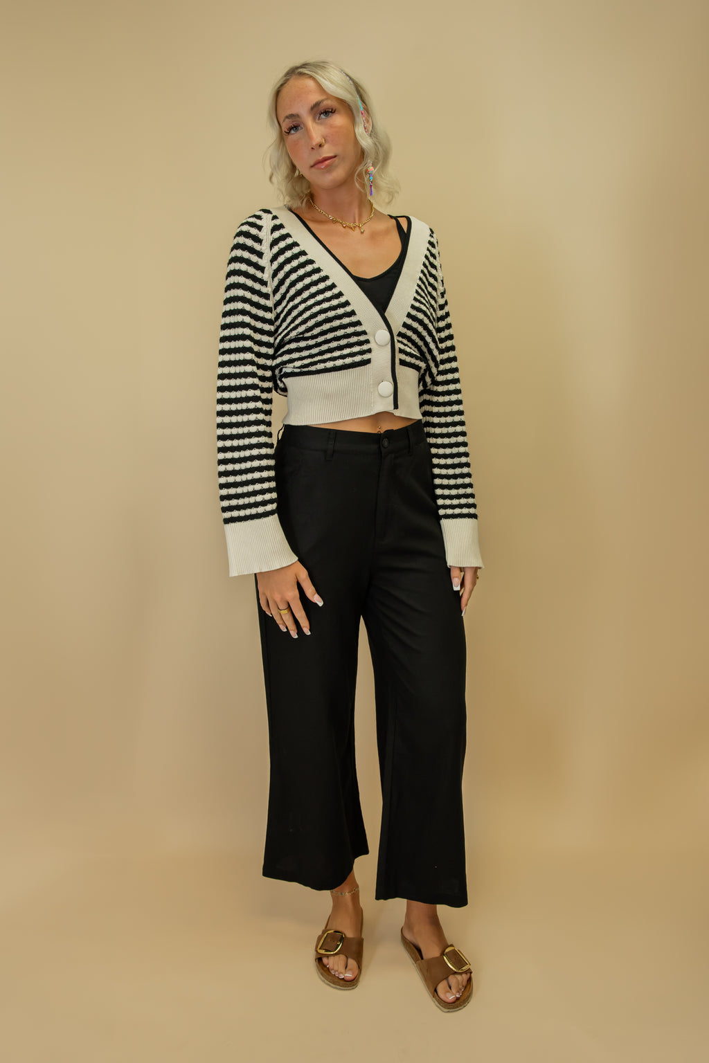 Woman wearing a black and white striped cardigan over a black top and pants on a beige background
