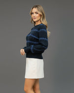 Person wearing a blue patterned sweater and white skirt on a beige background