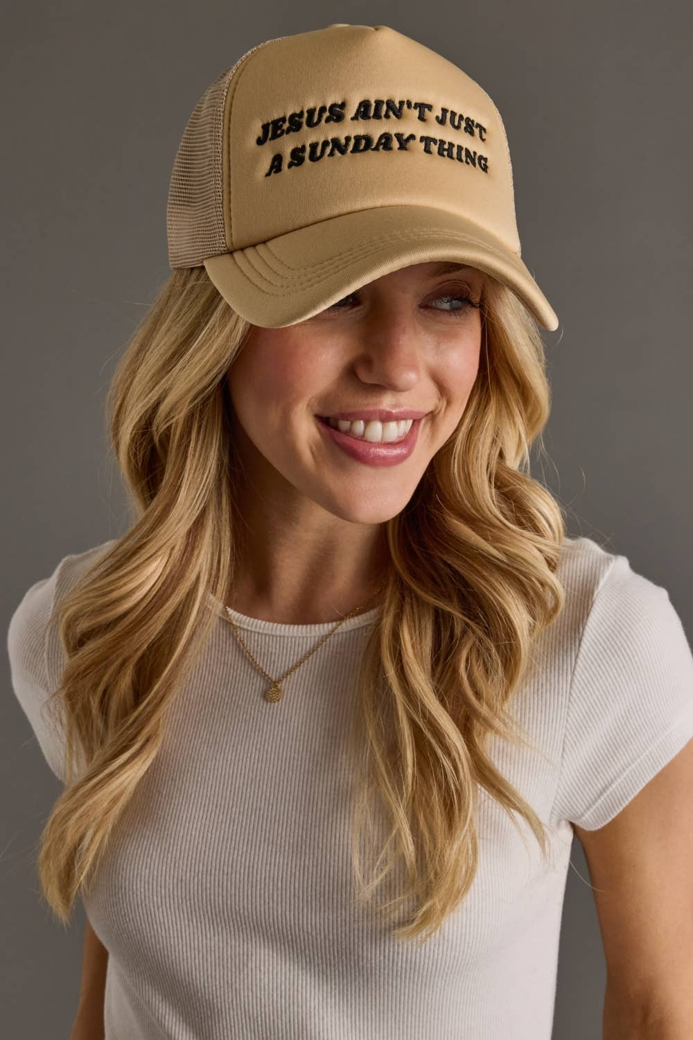 Woman wearing a beige cap with text, smiling against a gray background
