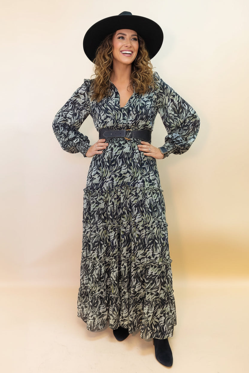Woman wearing a long patterned dress with a belt and black hat on a beige background