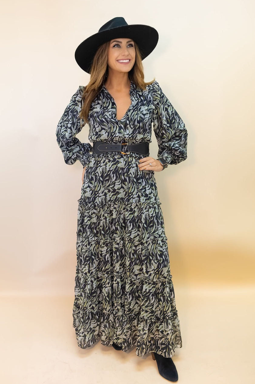 Woman wearing a long patterned dress with a belt and black hat on a beige background