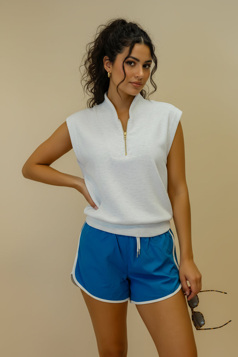 Woman wearing a white sleeveless top and blue shorts against a beige background