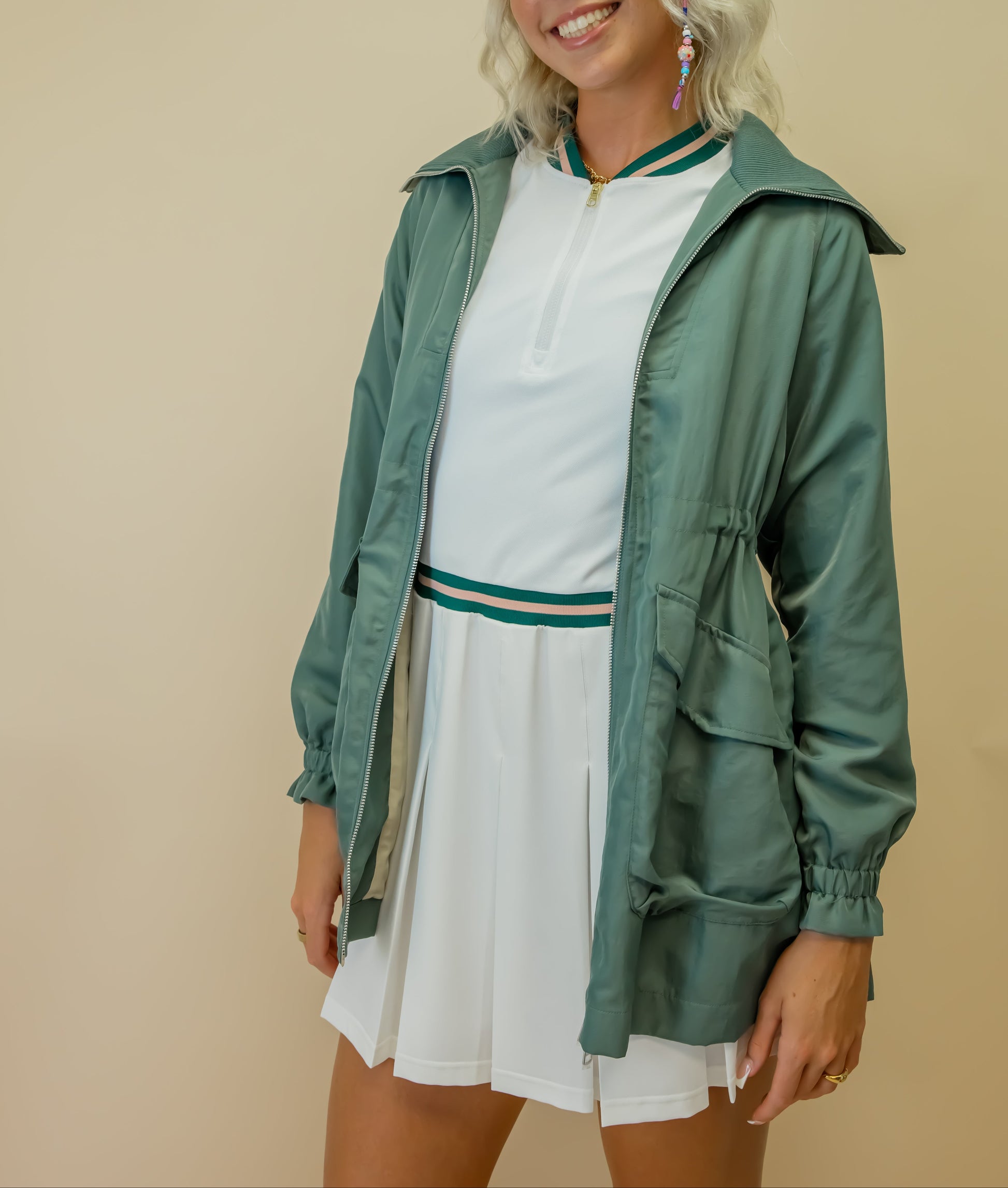 Woman wearing a green jacket over a white dress on a beige background