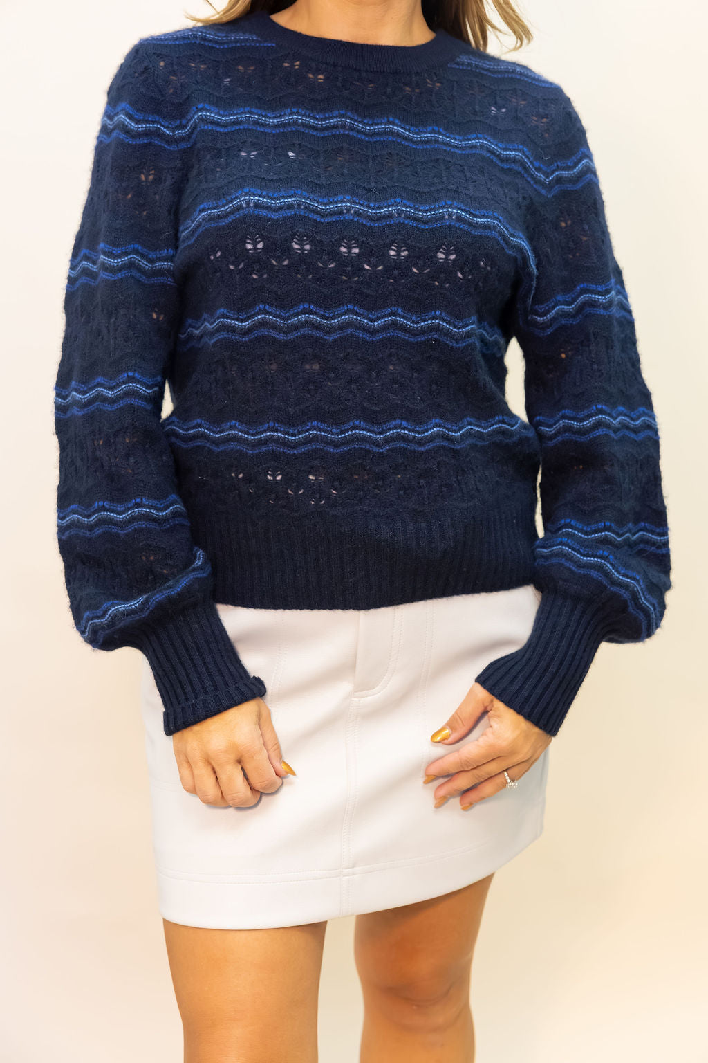 Person wearing a blue patterned sweater and white skirt on a beige background