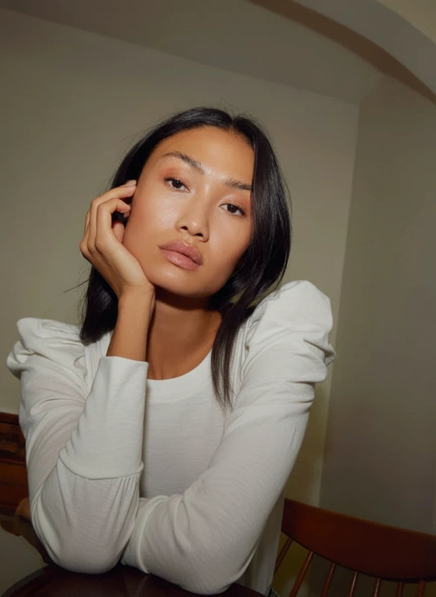 Woman wearing a white  long-sleeve top against a neutral background