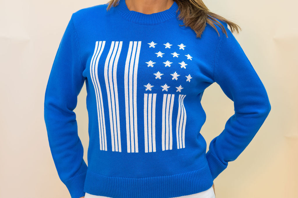 Blue sweater with American flag design worn by a person on a beige background