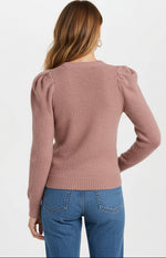 Person wearing a pink sweater with ruffled shoulders and blue jeans on a white background