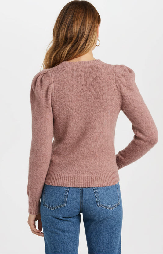 Person wearing a pink sweater with ruffled shoulders and blue jeans on a white background