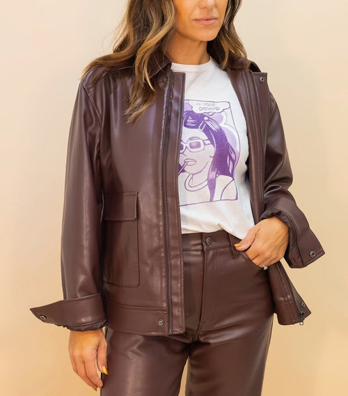 Woman wearing a brown leather jacket and pants with a graphic t-shirt on a beige background